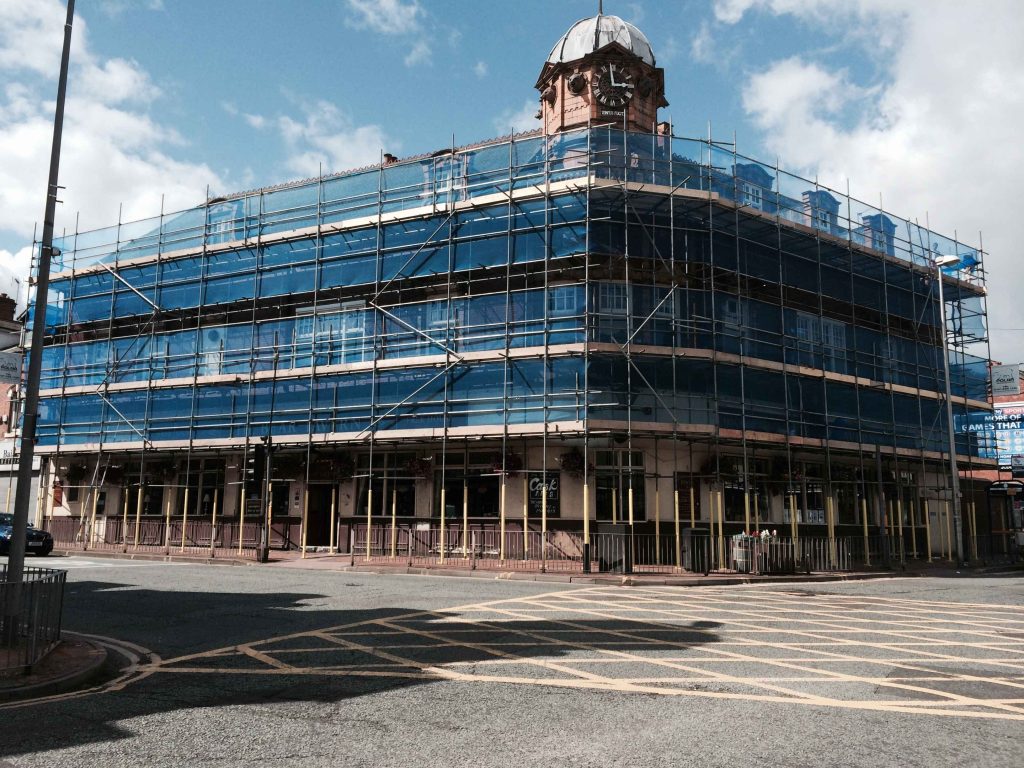 Blue scaffolding surrounding a multi-storey building under construction on a busy site